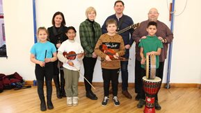 Several adults with a group of children holding various musical instruments.