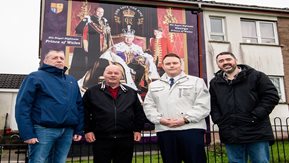 A group of men stand in front of a mural of the king of England. 