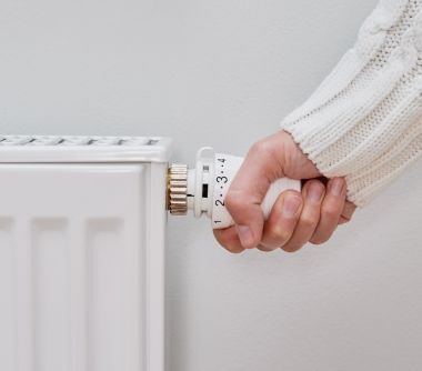 A hand turns down the heat of a radiator.