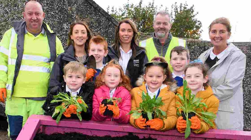 At the planters on Rathbrady Road are (back row): Chris McLaughlin, Causeway Coast and Glens Borough Council, Alana Donnelly and Martina Forrest, Housing Executive Patch Managers, Stephen Proctor, Causeway Coast and Glens Borough Council, and teacher, Mrs Casey, with some of the children from Termoncanice Primary School.