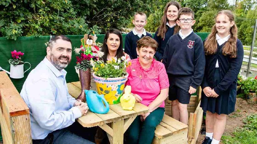 From L-R: Housing Executive Good Relations Officer Stephen Gamble, Mrs Kearney, teacher at St Oliver Plunkett, Una Johnston, Director of TIDAL Toome, and schoolchildren Mark, Grace, Eoin and Mya at the wooden boat seat in the kiddies’ cottage garden