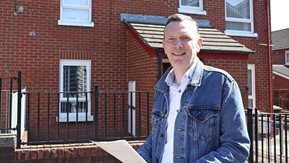 A smiling man stands outside a red brick end terrace house.