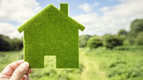 A hand holds a small house shaped prop.