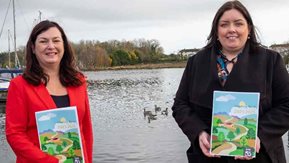 Two women stand by the side of a lake.