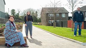 Three people pose in front of houses