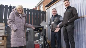 A woman and two men point at a new heating boiler.