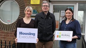 Louise Smyth, Eoin McKinney, and Ruth Buchanan with Housing Executive and sustainable rural communities graphics.