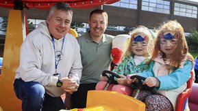 Two men smile while two young girls sit at driving wheel in toy car 