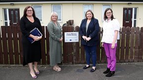 Four women stand in front of a bungalow