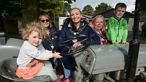 A group of women and children pose with a tractor at a community engagement day
