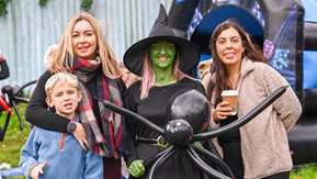 A group of women and a little boy pose with a woman dressed as a witch while they enjoy a Halloween party