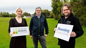 Three people, two hold Sustainable Rural Communities and NIHE placards
