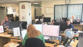 Staff in an office answer calls and work at personal computers.
