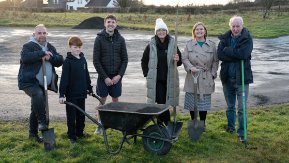 A group of people stand with gardening tools at the heart of Armoy village