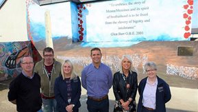 A group of people stand in front of a mural.