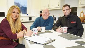 Two men and a woman drink tea at a kitchen table.