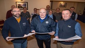 A group of men stand reading documents for a community information day