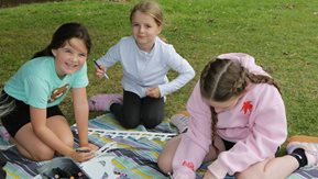 Three young girls enjoy their artwork outdoors.