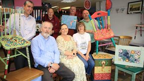 A group of men and women pose with artwork and restored furniture.