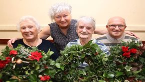 Four older men and women pose with a Christmas wreath.