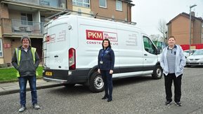 Three people stand in front of a contractor's white van