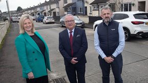 A woman and two men with a street of houses behind them.