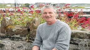 A man sits in front of a wall of flowers 