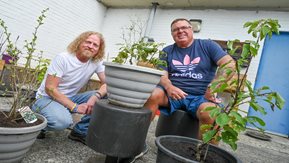 Two men sit beside potted plants