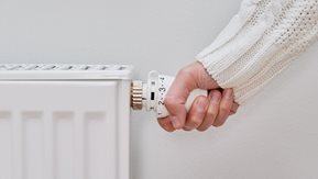 A hand turns down the thermostat on a radiator.
