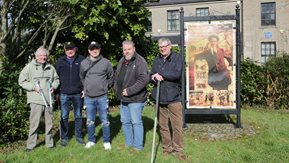 Several men, with gardening tools, stand in a garden.