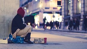 A homeless person sits on a street corner.