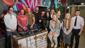 group of young people pose beside DJ mixing desk