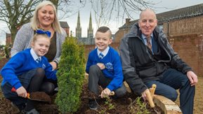 Two adults and two children planting shrubs in bedding plants.