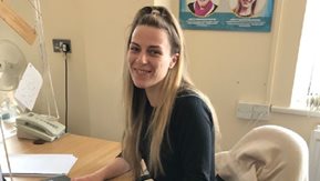 Young woman sits at a desk, smiling.