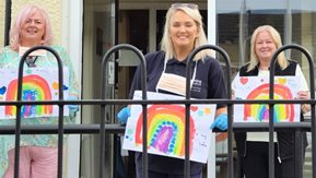 Three women hold paintings of rainbows.