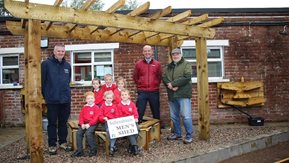 Three men stand beside six seated school children who are holding a Ballynahinch Men's shed placard.